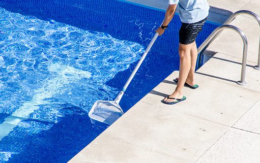 Person reinigt einen Swimmingpool mit einem Kescher.